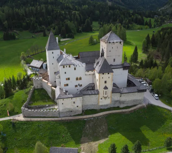 Castello medievale con torri bianche circondato da colline verdi e foresta